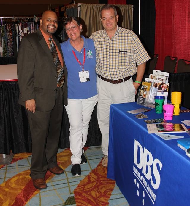 DBS Employees Robert Doyle, Kathy Acevedo and Ted Pobst standing in front of the DBS exhibit table.